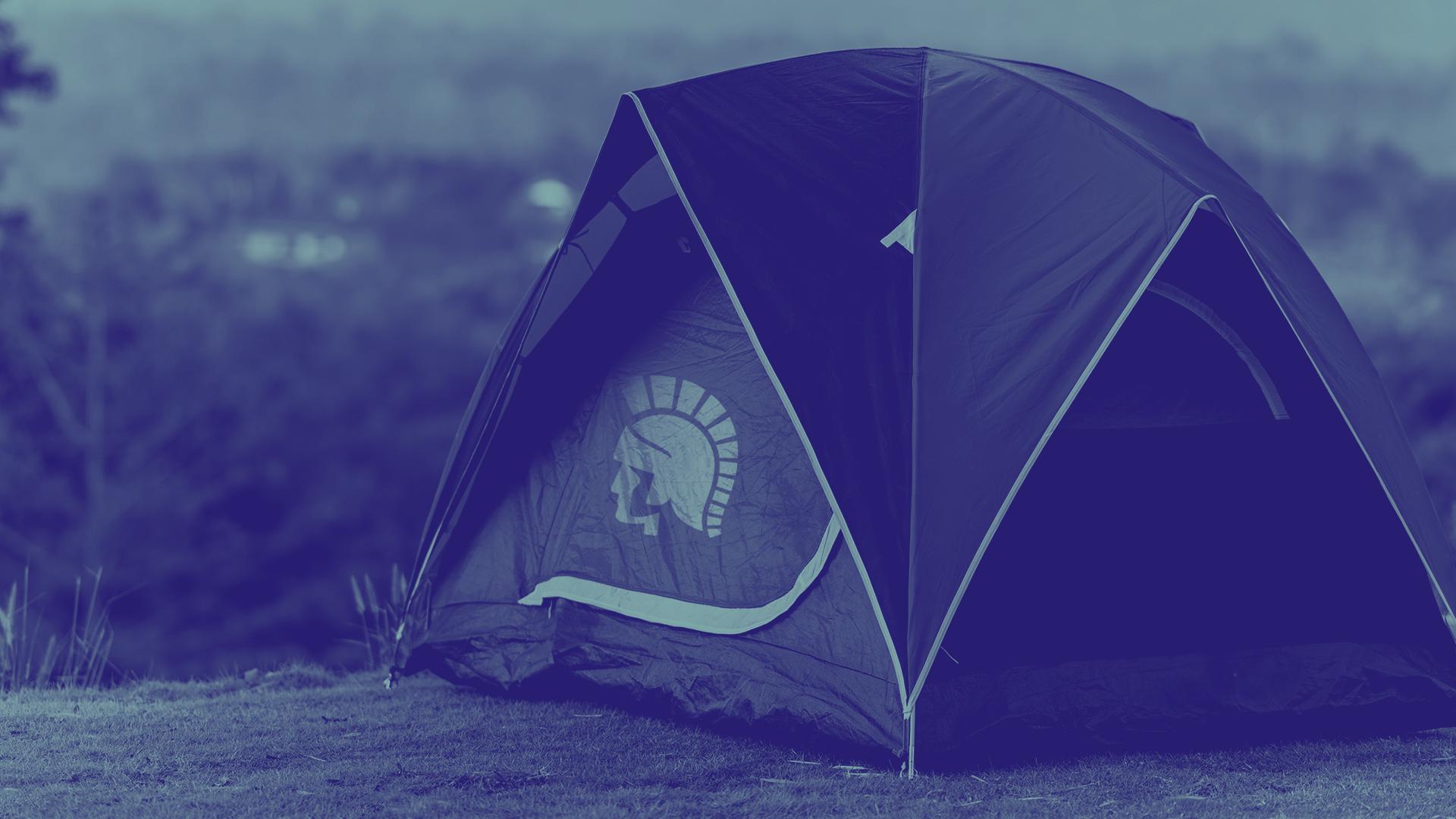 A tent with the Trojan logo on the front set up in a camp ground.