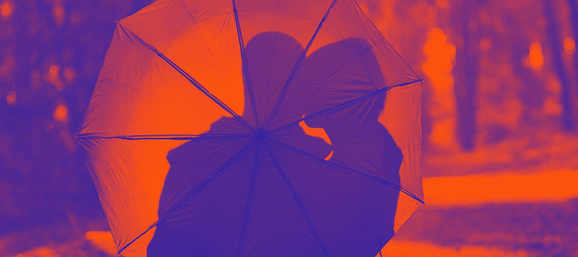 A couple making out under an umbrella.