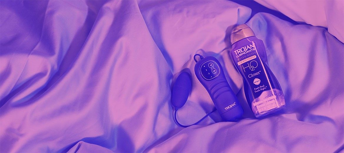 Trojan™ remote control vibrator and water based lube on a bed.