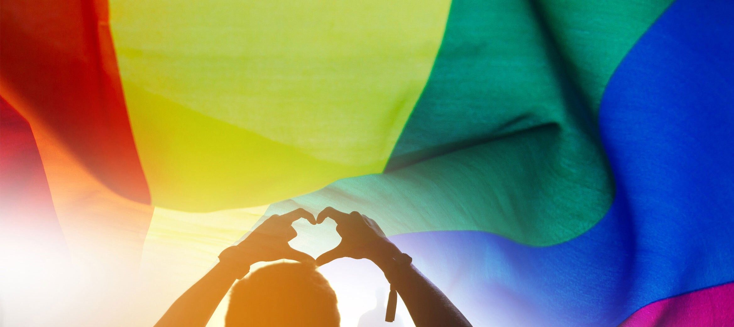 Person holding hands in heart shape over rainbow flag.